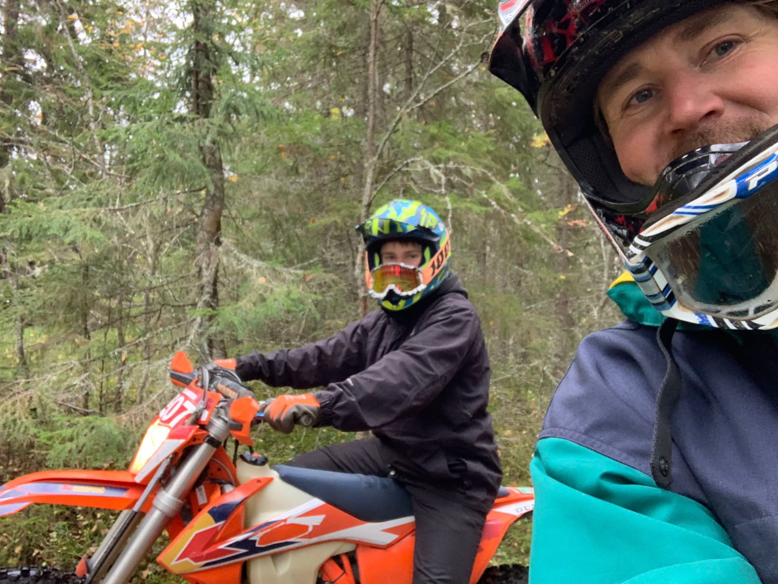 Zwei Personen mit Schutzhelmen und einem Motorrad im Wald